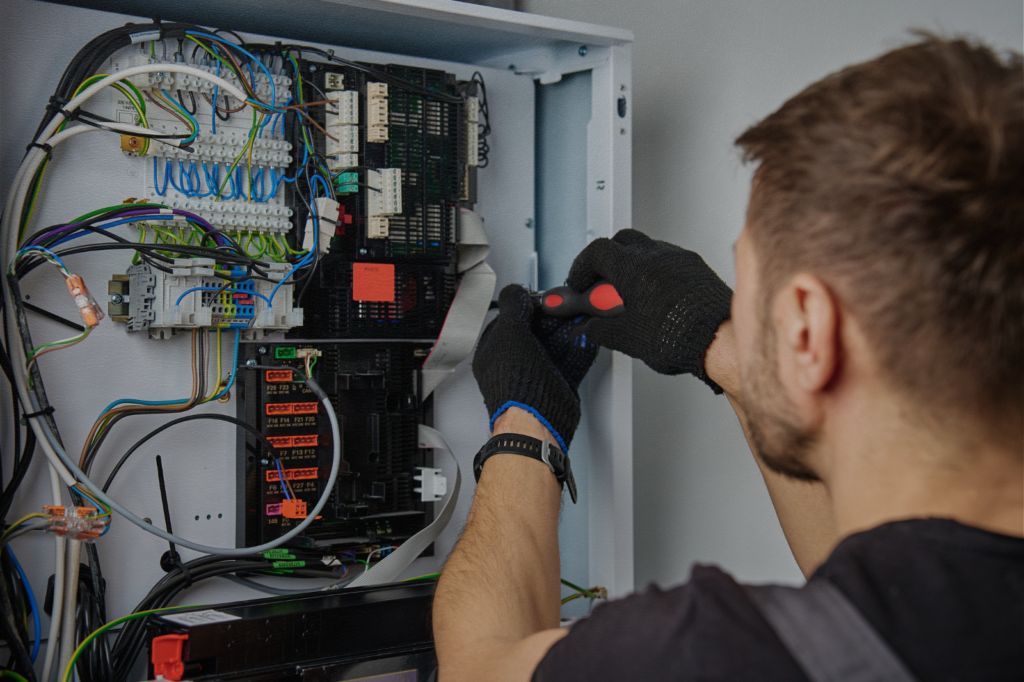 Technician inspecting a variable frequency drive inside an industrial control panel, showing wiring, circuit boards, and components commonly associated with VFD failures.