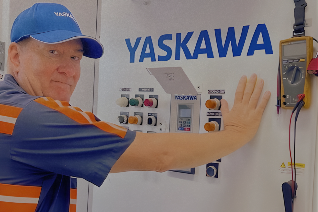 Technician inspecting a Yaskawa variable frequency drive installed in an industrial control panel.